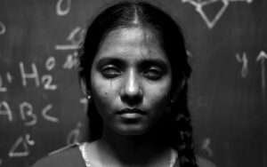 Black and white portrait of a young girl with her eyes closed, standing in front of a chalkboard filled with mathematical symbols and equations