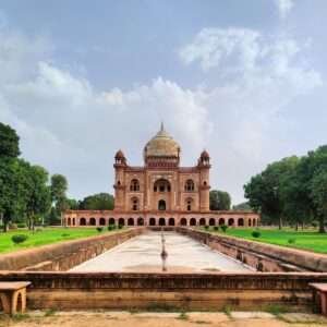 This photograph features the stunning architectural grandeur of Safdarjung's Tomb in Delhi, India. The tomb showcases intricate sandstone and marble craftsmanship with symmetrical design accentuated by the reflecting water channel leading up to the entrance.