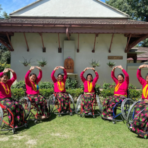 This image portrays a group of women in wheelchairs dressed in vibrant traditional attire. Their radiant smiles and synchronized poses convey a sense of unity, celebration, and empowerment.