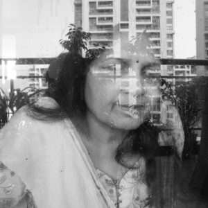 his black-and-white photograph captures a woman’s face reflected on a glass surface, creating a layered and abstract effect with the tall buildings in the background. The interplay of reflections and transparency evokes a sense of introspection or connection between the subject and her surroundings.