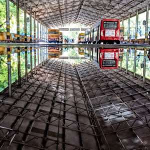 This photograph captures a symmetrical view of the bus terminal mirrored perfectly in a puddle of water on the ground. The image conveys a sense of order and balance in a bustling transit space, reflecting the stillness and depth to be found in a busy space.