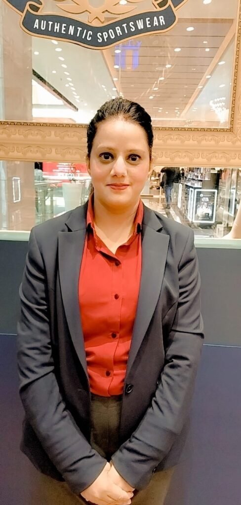 Rishu Bhardwaj, a deaf retail professional, confidently dressed in a red shirt and blazer, standing at her workplace.