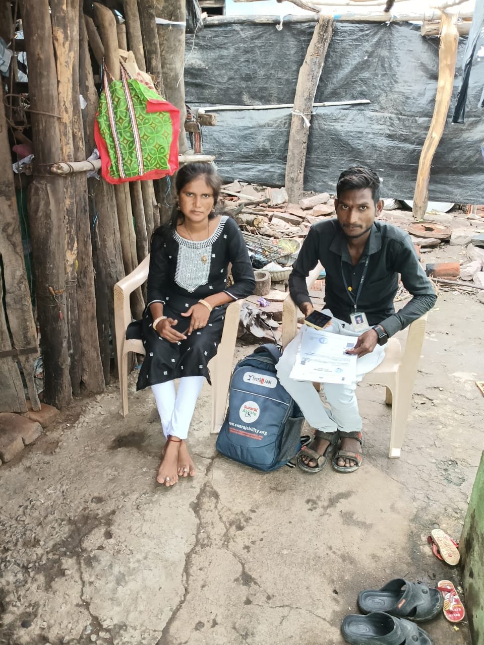 Kishore, grassroot fellow, seated beside a woman outside a rural home, helping her with UDID card application documents