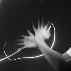 A pair of hands captured in motion in a dark space, with bright light trails creating sweeping curves around them.