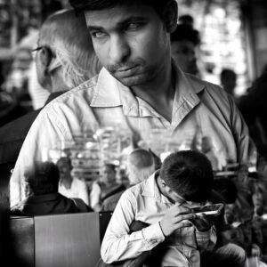 A double-exposure black-and-white portrait of a man looking thoughtfully to the side, layered over a scene of people sitting closely together.