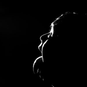 A dramatic black-and-white silhouette of a person’s side profile, their face lit softly against a dark background.