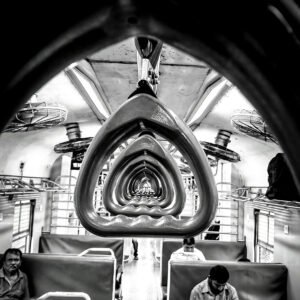 A black-and-white photo of a train interior, focusing on the hanging hand grips that form a repeating triangular pattern down the aisle.
