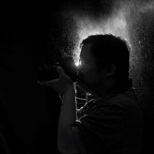 A silhouette of a photographer taking a picture, with light shining through mist behind them
