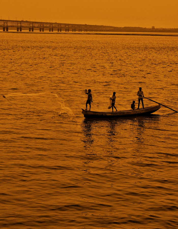 Fishermen casting their nets in the twilight glow of the Godavari River, with the bridge elegantly silhouetted in the background.